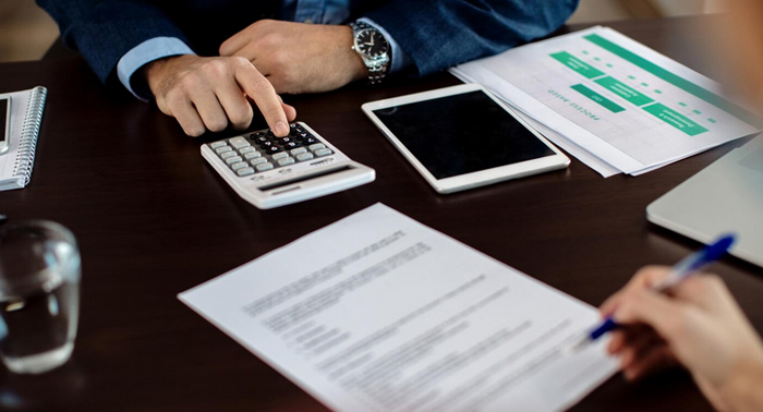 Person calculating finances with a calculator and reviewing documents related to payday loans, emphasizing cash flow management in San Jose.