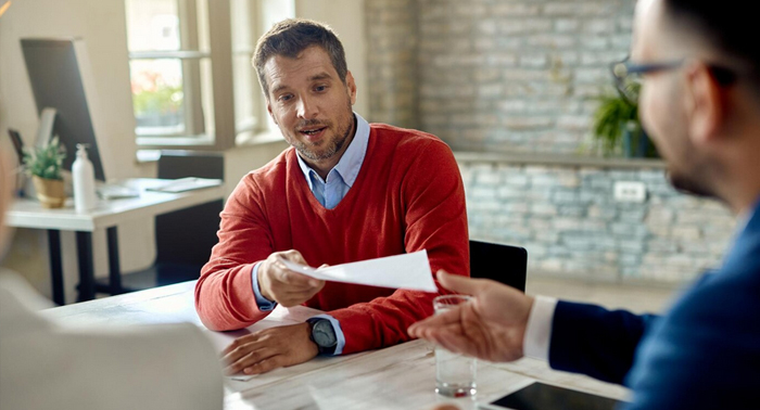 Man in a red sweater discussing financial documents with another person at a table, representing the process of applying for payday loans.